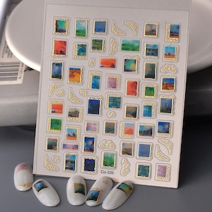 May include: A sheet of nail art stickers featuring miniature landscape paintings in gold frames. The paintings display various scenes with colorful skies and landscapes. The text "Co-326" is visible on the sheet. Several decorated nails are also present.