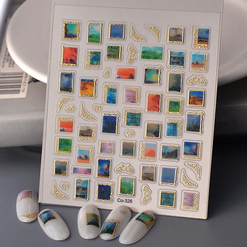 May include: A sheet of nail art stickers featuring miniature landscape paintings in gold frames. The paintings display various scenes with colorful skies and landscapes. The text "Co-326" is visible on the sheet. Several decorated nails are also present.
