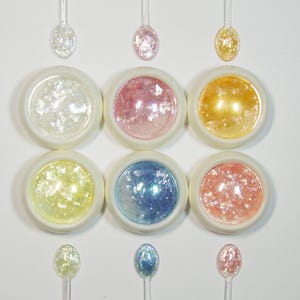May include: Six small jars of iridescent glitter in various colours, including white, pink, gold, yellow, blue, and peach. Each jar has a small spoon for scooping the glitter.