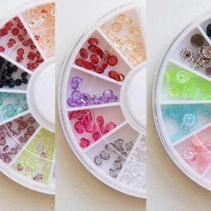 May include: A set of three nail art wheels with different colored rhinestones and other embellishments. Each wheel has 12 compartments, each filled with a different type of embellishment.