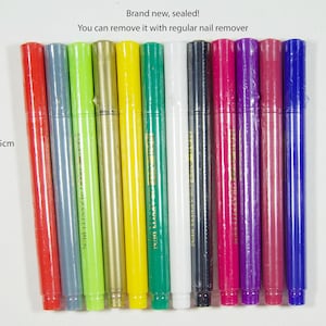 May include: A set of 12 colorful markers, each 13.5 cm long, with a black cap and a gold label. The markers are brand new and sealed. The text "Brand new, sealed! You can remove it with regular nail remover" is printed on a white background.