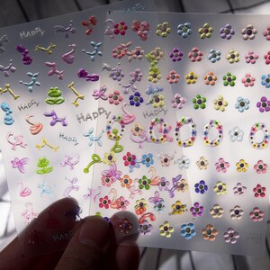 May include: A sheet of colorful stickers with various designs, including flowers, animals, and the word "Happy".
