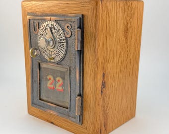 May include: A wooden box featuring a vintage-style metal post office door on the front. The door has a circular combination dial with letters A through L, the letters U and S, and a glass window displaying the red number 22 inside a metal frame.