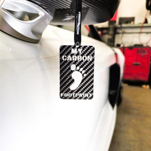 May include: A black carbon fiber car air freshener with a white footprint and the text "MY CARBON FOOTPRINT".