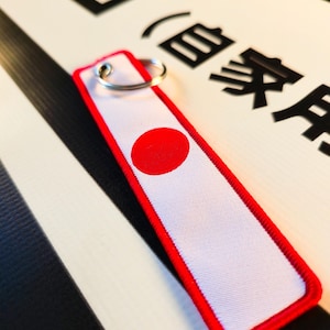 Etiqueta con la bandera japonesa JDM, llavero con etiqueta de vuelo de Japón, llavero de tela para motocicleta, correa de muñeca con etiqueta de avión para coche importado, accesorio para llavero de motociclista