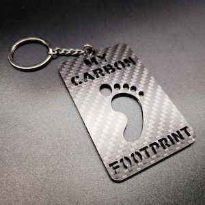 May include: A silver keychain with a carbon fiber design. The keychain has a footprint cutout and the text "MY CARBON FOOTPRINT".