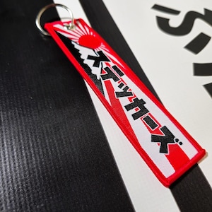May include: Red, white and black keychain with a Japanese mountain and sun graphic. The text "JDM" is written in Japanese on the keychain.
