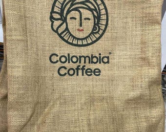 Könnte beinhalten: Ein brauner Jutesack mit einem schwarz-weißen Logo eines Frauenkopfes mit dem aufgedruckten Text "Colombia Coffee".