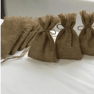 Puede incluir: Un conjunto de pequeñas bolsas de arpillera marrón con cierre de cordón. Las bolsas están hechas de tela de arpillera natural y tienen un aspecto rústico y hecho a mano.