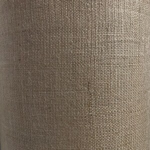 May include: A close-up of a brown burlap fabric with a rough texture. The fabric is woven with a tight weave and has a natural, rustic look.