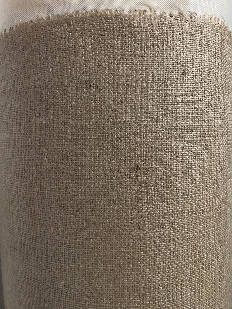 May include: A close-up of a brown burlap fabric with a rough texture. The fabric is woven with a tight weave and has a natural, rustic look.
