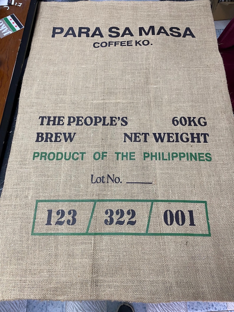 May include: A brown burlap sack with black text that reads "PARA SA MASA COFFEE KO. THE PEOPLE'S BREW 60KG NET WEIGHT PRODUCT OF THE PHILIPPINES Lot No. 123 322 001".