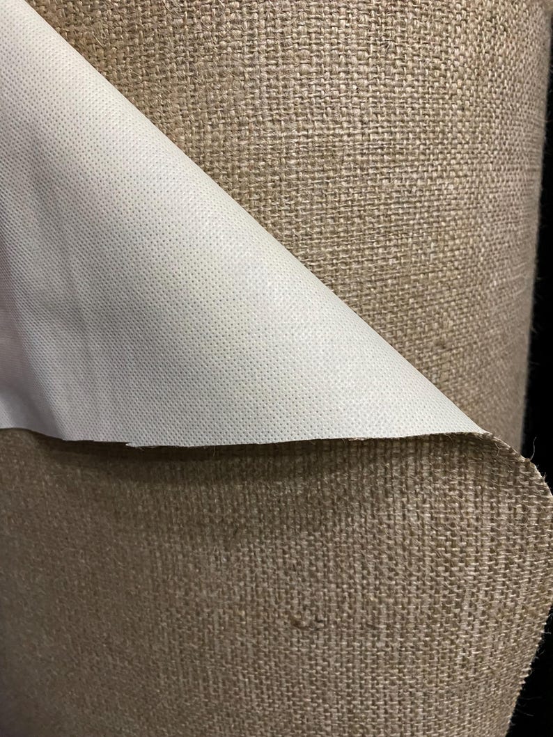 May include: Close-up of a roll of brown burlap fabric with a white backing. The burlap has a woven texture and the backing is smooth.