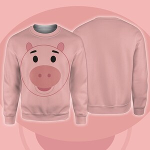 Pode incluir: Um moletom rosa claro com o rosto de um porco de desenho animado na frente. O rosto do porco tem olhos pretos, um focinho rosa e orelhas rosas. A parte de tr&aacute;s do moletom &eacute; de cor rosa claro lisa.