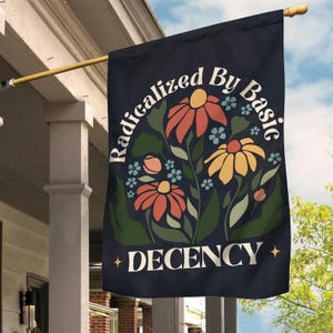 May include: A navy blue flag with a white circle containing the text "Radicalized By Basic Decency" and a floral design with red, yellow, and pink flowers.