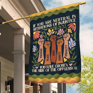 May include: A blue flag with a floral design and the text "If you are neutral in situations of injustice, you have chosen the side of the oppressor." The text is surrounded by raised fists with words like "freedom", "peace", "hope", "dignity", and "equality" written on them.