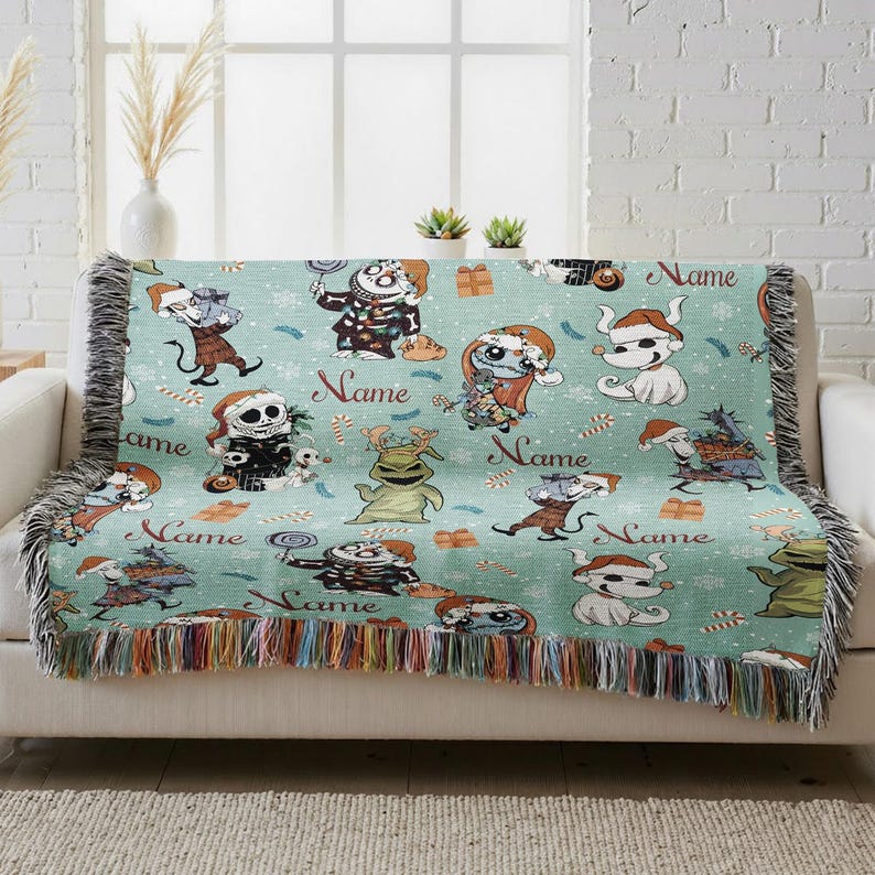 A colorful throw blanket with various cartoon characters and the word "Name" printed on it, placed on a couch in front of a window.