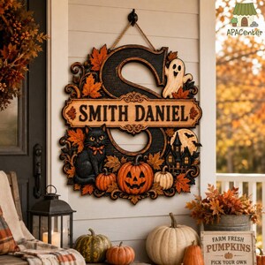 May include: A decorative wooden wall sign featuring a large black letter S, a black cat, a jack-o'-lantern, a ghost, and a haunted house. The sign displays the text SMITH DANIEL on a central horizontal plaque, surrounded by orange autumn leaves.