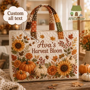 May include: A quilted tote bag featuring a cream background with a printed autumn harvest pattern of sunflowers, pumpkins, and fall foliage. The text 'Ava's Harvest Bloom' is embroidered on the front. It has two patterned fabric handles.