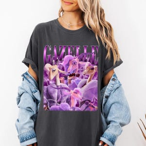 A woman wearing a black t-shirt with a graphic design featuring purple and pink cartoon-like characters.