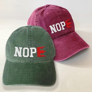 Two baseball caps, one green and one maroon, with the word "NOP" printed on them.