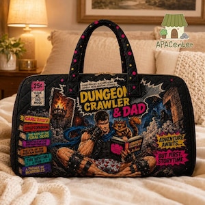 May include: A black quilted fabric bag featuring a comic book style graphic of a character reading to a cat. The text reads Dungeon Crawler & Dad, Adventure Awaits, But First Storytime, and lists various book titles on the left side of the bag.