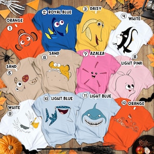 May include: A collection of colorful t-shirts featuring cartoon sea creatures. Colors include orange, blue, yellow, white, pink, and light blue. Each shirt has a unique character design, perfect for fans of animated movies.