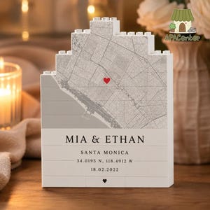 May include: A white building block display featuring a gray map of Santa Monica with a red heart marker. The text reads MIA & ETHAN, SANTA MONICA, 34.0195 N, 118.4912 W, and 18.02.2022, with a small black heart icon at the bottom center.