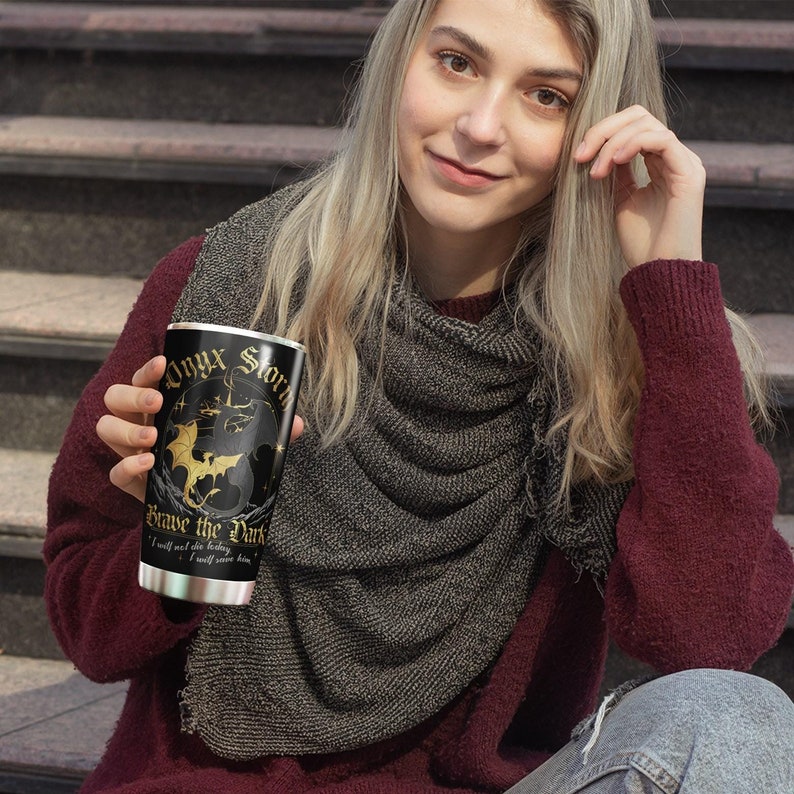 May include: A black and gold stainless steel tumbler with the text "Onyx Storm" and "Brave the Dark" and a graphic of a dragon. The text "I will not fear the fading light, I will save him." is also on the tumbler.