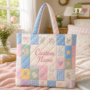 Puede incluir: Un bolso tote acolchado con un diseño de patchwork de cuadrados en azul pastel, rosa, amarillo y verde. La tela muestra patrones de flores, lazos, estrellas, corazones y un conejo. El panel central presenta el texto bordado Custom Name.