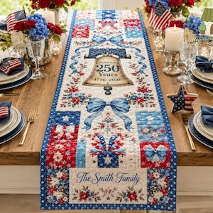 May include: A patriotic table runner with a red, white, and blue color scheme. The runner features a design with the Liberty Bell, bows, and floral patterns. The text reads "Celebrating 250 Years 1776-2026" and "The Smith Family".
