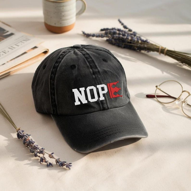 a black baseball cap with the word "NOP" printed on it, placed on a table alongside a pair of glasses, a newspaper, and some lavender flowers.