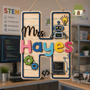 May include: A large wooden letter H wall hanging featuring the text Mrs. Hayes in black script and colorful block letters. The design includes a grey robot, a yellow lightbulb, green and blue gears, a laptop, and a code bracket symbol.