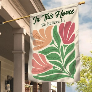 May include: A beige flag with green and pink floral designs. The text "In This Home We Believe In" is at the top of the flag. The flag lists values such as love, peace, hope, religious freedom, truth in science, equality for all, respect for disabilities, kindness, diversity and inclusion, people and planet over profit, love is love, women's rights, and human rights.