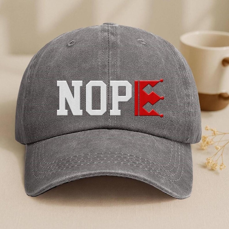 A gray baseball cap with the word "NOPE" printed on it, along with a red flag-like symbol.