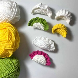 K&ouml;nnte beinhalten: Eine Sammlung bunter geh&auml;kelter Kn&ouml;del in verschiedenen Farben, darunter Wei&szlig;, Gelb, Gr&uuml;n und Pink. Die Kn&ouml;del sind auf einer wei&szlig;en Oberfl&auml;che angeordnet.