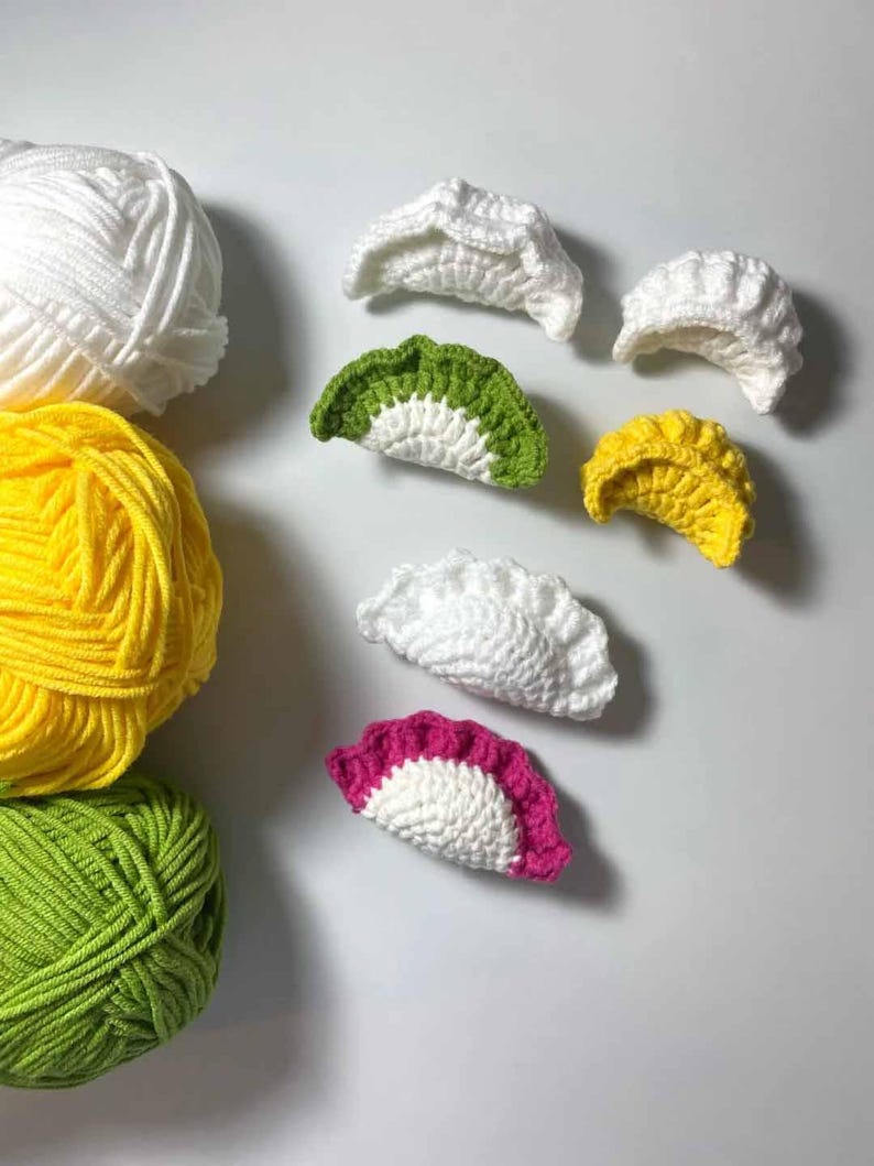 K&ouml;nnte beinhalten: Eine Sammlung bunter geh&auml;kelter Kn&ouml;del in verschiedenen Farben, darunter Wei&szlig;, Gelb, Gr&uuml;n und Pink. Die Kn&ouml;del sind auf einer wei&szlig;en Oberfl&auml;che angeordnet.