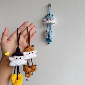 May include: Crocheted ghost and bear-themed hanging ornaments in white, black, brown, and yellow. One ghost wears a witch hat and holds a yellow heart. The other has bear ears. A blue sea creature ornament hangs on the wall.