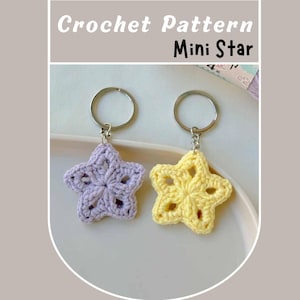 May include: Two crocheted star-shaped keychains, one purple and one yellow, hanging from silver key rings. Crochet pattern mini star.