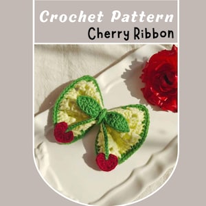 May include: A crocheted cherry ribbon bow with green leaves and red cherries. The bow is on a white plate.