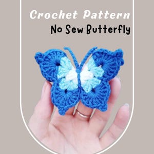 Puede incluir: Una mariposa de ganchillo hecha a mano en tonos azules y blancos. La mariposa se sostiene en una mano y presenta intrincados patrones de alas. El texto en la parte superior dice "Crochet Pattern" y "No Sew Butterfly".