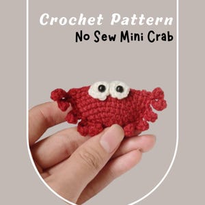 Puede incluir: Un pequeño cangrejo rojo tejido a ganchillo con ojos blancos y negros se sostiene en una mano. El cangrejo tiene una apariencia texturizada y está etiquetado como "Crochet Pattern No Sew Mini Crab" en texto blanco.