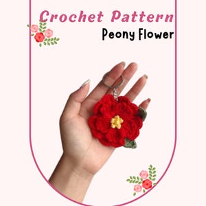 May include: A red crochet peony flower keychain with a yellow center and green leaves. The keychain is held in a hand. Text at the top reads "Crochet Pattern Peony Flower".