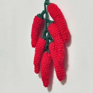 May include: A bunch of crocheted red chili peppers with green stems hanging from a string.