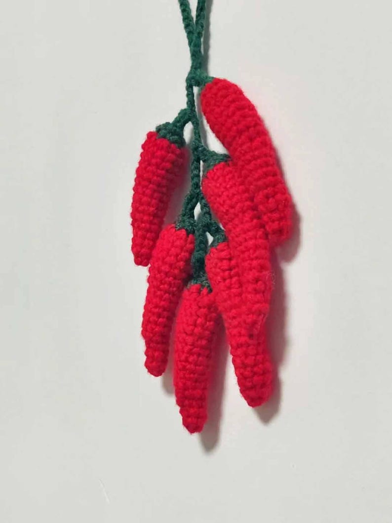 May include: A bunch of crocheted red chili peppers with green stems hanging from a string.