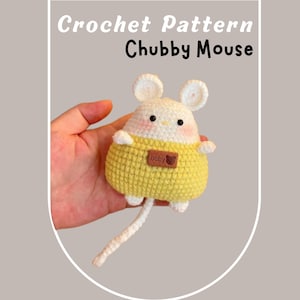 May include: A crocheted stuffed mouse with a white body, yellow sweater, and a brown tag that says "baby" with a heart. The mouse has a long white tail.