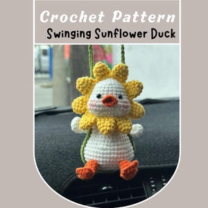 May include: A crocheted sunflower duck car charm. The duck has a white body, yellow sunflower petals, and orange feet and beak. The text "Crochet Pattern Swinging Sunflower Duck" is at the top of the image.