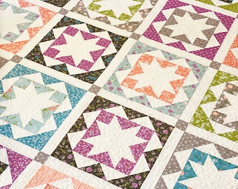 May include: A quilt with a patchwork design featuring a variety of floral prints in shades of pink, green, blue, and purple. The quilt is made up of squares with a white star in the center of each square. The quilt is quilted with a pattern of small hearts.