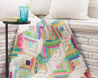 May include: A colorful patchwork quilt with a log cabin pattern in shades of pink, blue, green, and yellow. The quilt is made with a variety of fabrics, including floral prints and geometric patterns. The quilt is folded and displayed on a white couch with pillows.