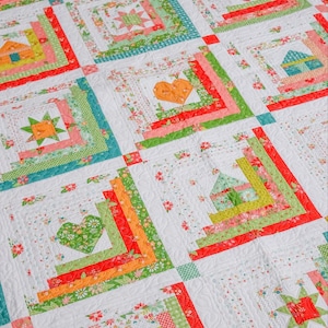May include: A colorful quilt with a log cabin pattern featuring various shapes, including hearts, stars, and houses. The quilt is made with a variety of fabrics in shades of red, orange, yellow, green, and blue.
